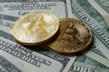 Two symbolic coins of bitcoin on banknotes of one hundred dollars.