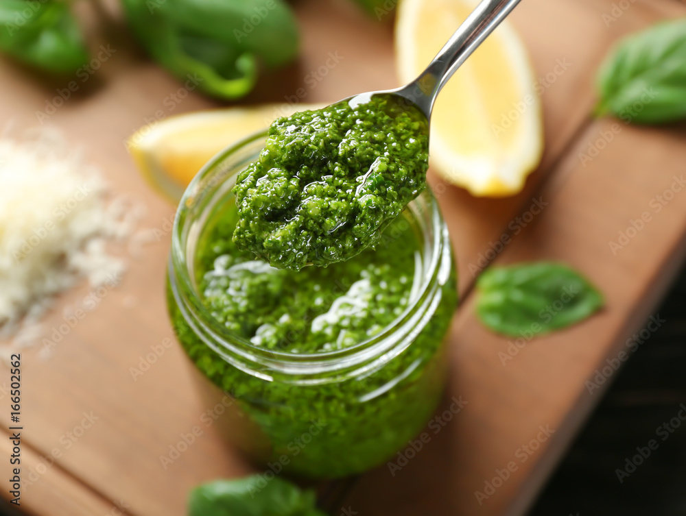 Spoon with delicious sauce over jar on wooden board