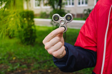 Young Man Holds A Spinner. Natural. Popular Spinner Gadget. Man Holds A Metal Gray Spinner.  Anti Stress And Relaxation Fidgets, Spinner For Tired People