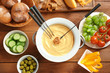 Cheese fondue in pot and different products on wooden table