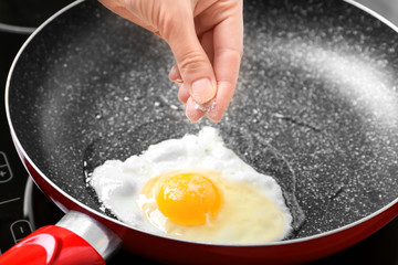 Sticker - Female hand adding salt to egg in frying pan