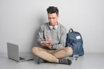 Young asian man in casual clothes is using a laptop, smiling while sitting on the floor