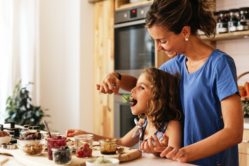 Wall Mural - Little girl cooking with her mother in the kitchen.