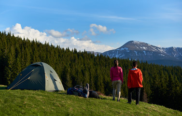 Full length shot of two female hikers with backpacks enjoying stunning view from the top of a hill near tents while camping and hiking in the mountains friendship achievement nature peaceful freedom.