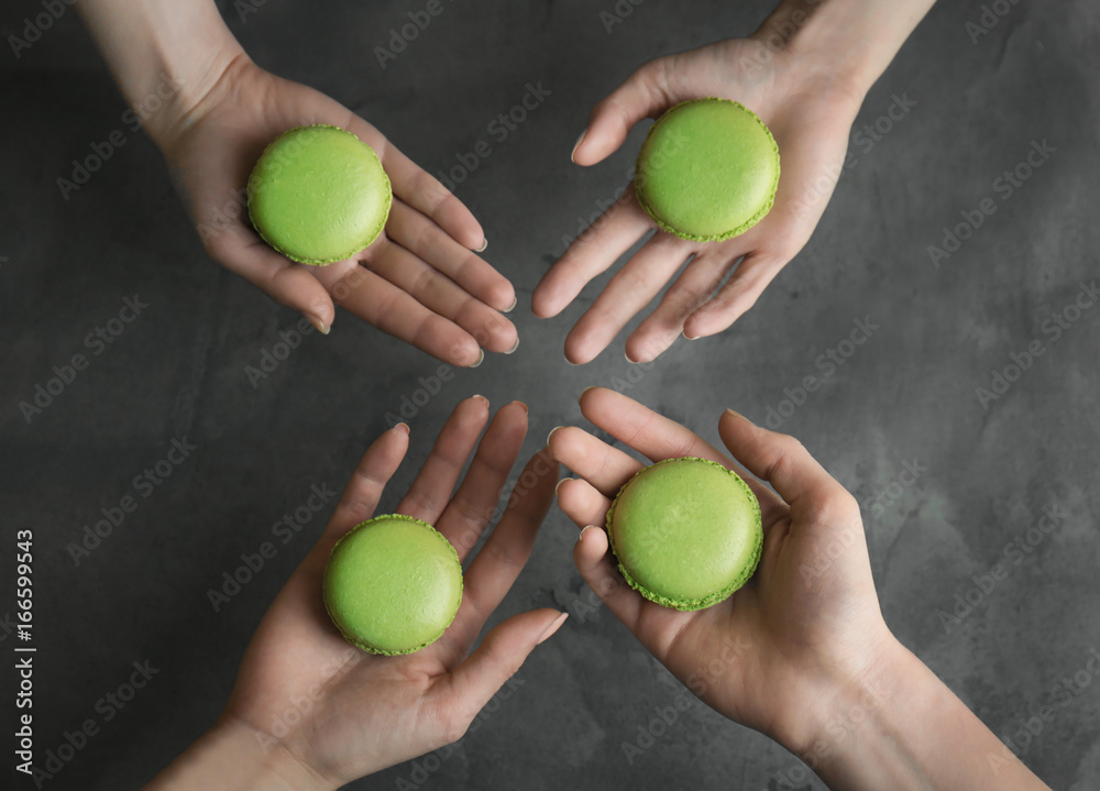 People holding tasty green macarons on gray background