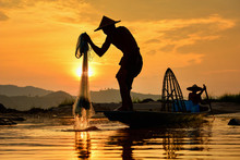 Silhouette Of Fishermen Lifting Fishing Net Out Of The River At Sunset, Thailand