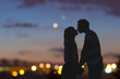 canvas print picture - Silhouettes of a young couple kissing with city panorama in the background.
