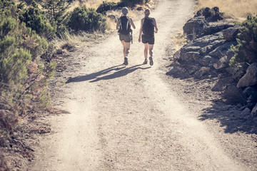 Two european women friends on trip in countryside, Way arid landscape with travelers, Tourists with backpack sporting in summer nature, Long trip in countryside with tramps, Young sporty women on trip