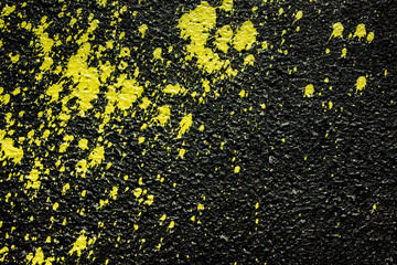 Yellow paint spray splash on black concrete wall background.