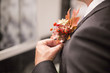 Groom attach flowers to the suit. man's hand adjusts the wedding boutonniere. Wedding boutonniere on a black tuxedo