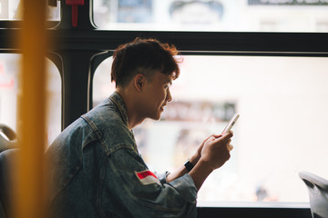 Handsome asian man sitting in city bus and typing a message on the phone.