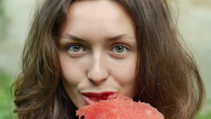 Wall Mural - Beautiful young woman is eating watermelon with pleasure and look at camera