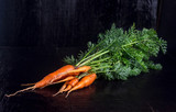 Fototapeta Tulipany - Carrots with a tops on a black wooden table