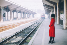 Young Beautiful Woman Curly Hair In A Red Coat And Russian Fur Hat On A Train Station