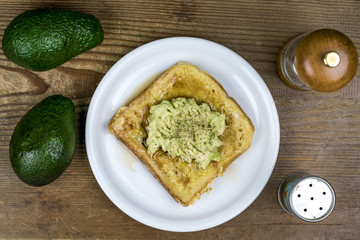 Fresh avocado pear sandwich with two whole fruit alongside and condiments viewed from above on wood