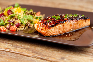 Grilled salmon with quinoa salad on brown plate.