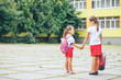 Two girls stand on the background of the school hand in hand. Schoolgirls view from the back