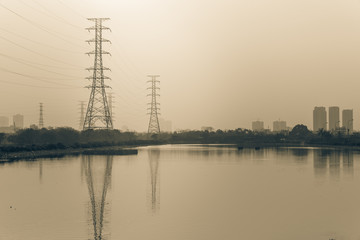 Wall Mural - Group silhouette of transmission towers (power, electricity pylon, steel lattice) by the lake at sunset in suburb Hanoi, Vietnam. Row of residential building complex in background. High voltage pillar