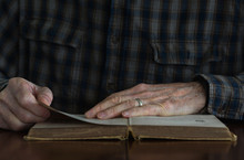 Close-up Of A Senior Man's Hands On The Pages Of An Old Book.