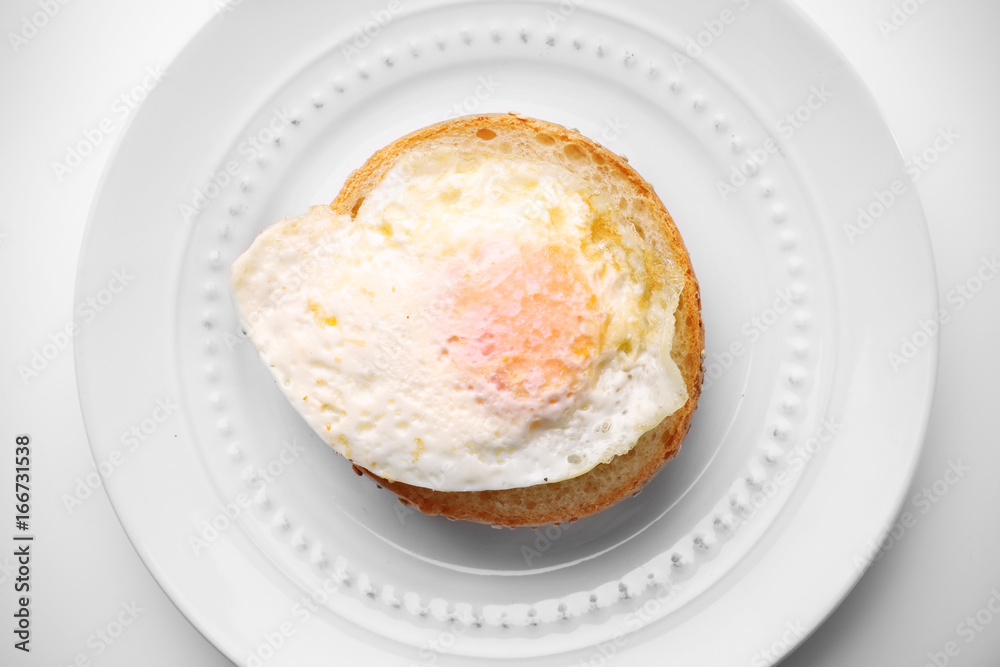 Ceramic plate with hamburger roll and over hard fried egg on light background