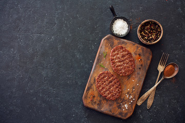 Two beefsteaks , peppers and old spoon, fork and cutting board over black stone background