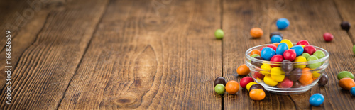 Plakat Portion of Cocolate coated Peanuts on wooden background (selective focus)