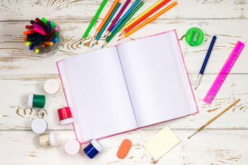 Wall Mural - Outdoor notebook surrounded by school supplies on a white wooden background with empty space for inscriptions.