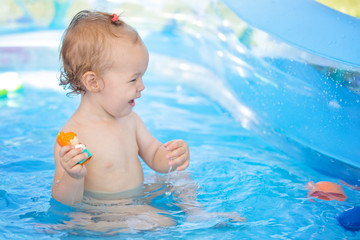 Wall Mural - Sixteen months old baby girl playing in the plastic pool with her toys; baby covered with sun protection cream; happy and care free childhood concept