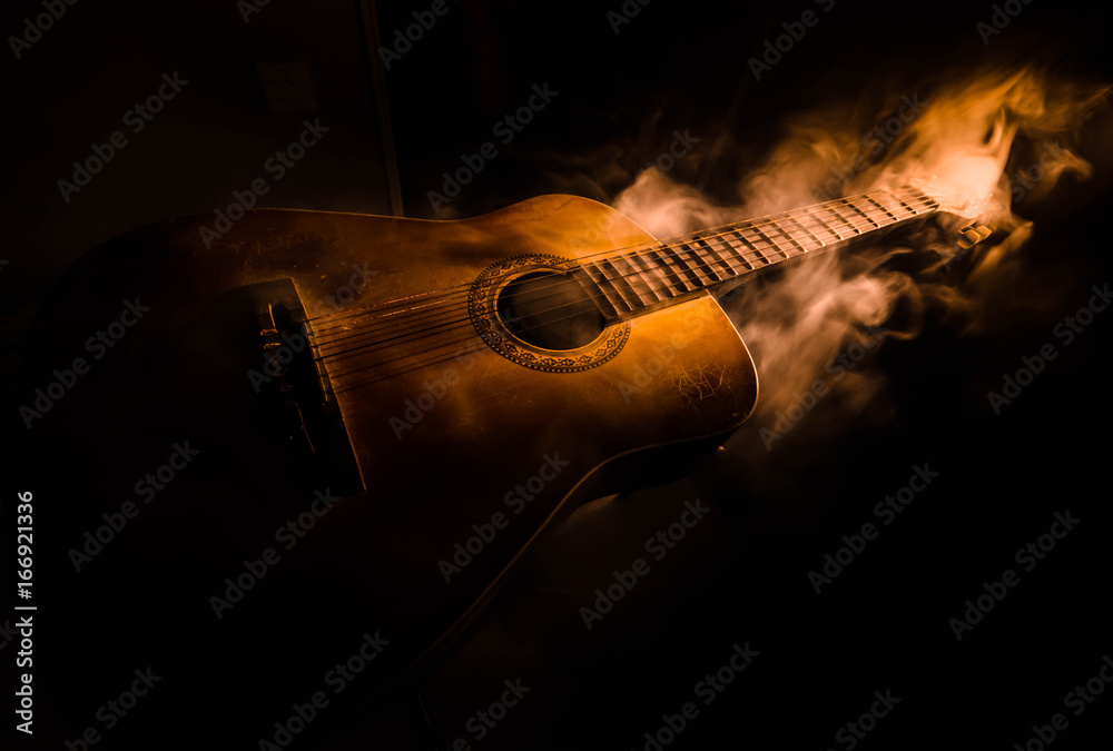 Music concept. Acoustic guitar isolated on a dark background under beam of light with smoke with copy space. Guitar Strings, close up. Selective focus. Fire effects - obrazy, fototapety, plakaty 