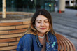© shurkin_son - Close up shot of gorgeous young Caucasian female wearing jeans jacket, earrings and nose-ring relaxing on wooden bench outdoors, looking down with cute shy smile. Urban style and fashion concept