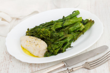 boiled fish with greens and olive oil on white dish on wooden background