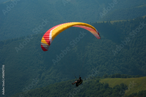 Fotografie, Obraz A paraglider flies over a mountain valley on a sunny summer day