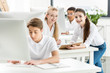 © LIGHTFIELD STUDIOS - smiling teenage girls looking at camera while sitting at table in classroom with classmates