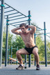 © undrey - Muscular fitness athlete doing squats with his hands behind the head exercising in the park.