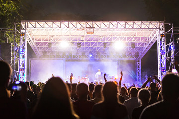 Rear view of crowd with arms outstretched at concert. cheering crowd at rock concert. silhouettes of concert crowd in front of bright stage lights. Crowd at music concert, audience raising hands up