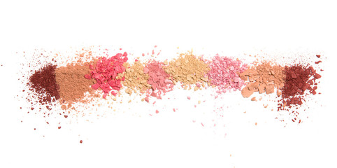 Samples of dry blush, powder, bronzers and highlighter scattered in a line isolated on a white background