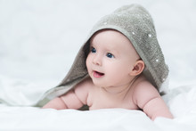 Cute Baby Girl Or Boy After Shower With Towel On Head In White Sunny Bedroom. Child With Big Blue Eyes Smiling And Relaxing In Bed After Bath Or Shower