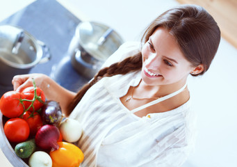 Wall Mural - Smiling young woman holding vegetables standing in kitchen