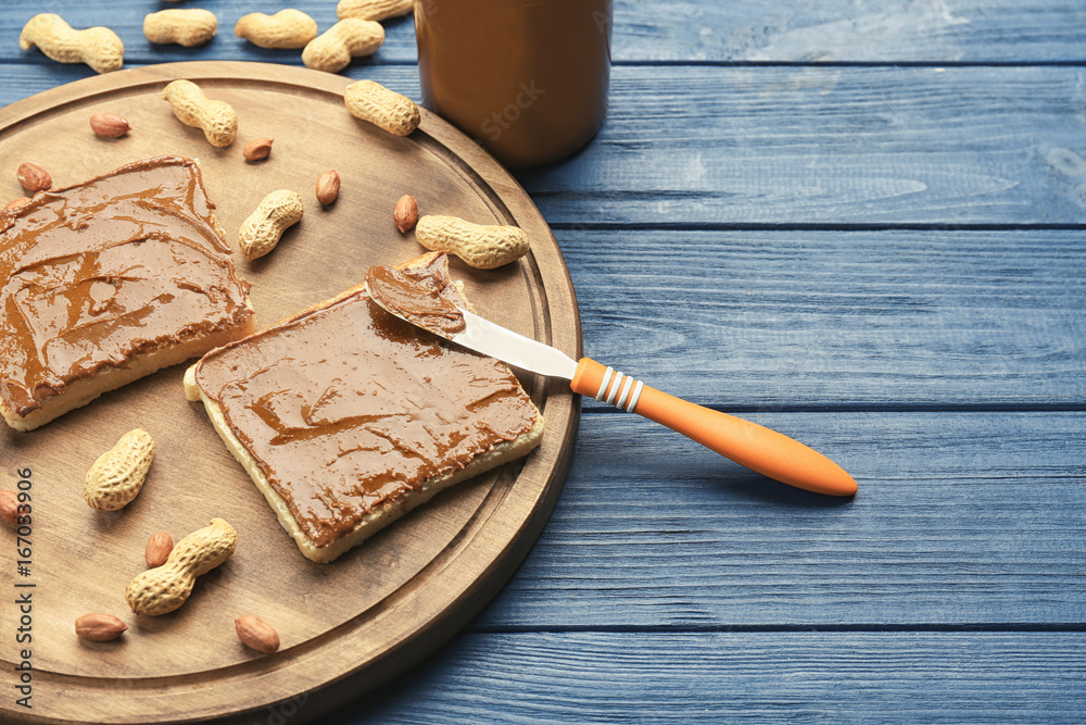 Toasts with delicious peanut butter, nuts and knife on wooden table
