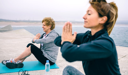 Wall Mural - Senior woman exercising with female coach in a concrete pier. Selective focus on woman in background