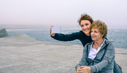 Wall Mural - Personal trainer taking selfie with senior woman by sea pier