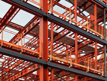 Metal Framework Of New Building Development With A Network Of Orange Steel Girders  And Safety Fencing