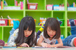 © weedezign - Two girl kid lay down on floor and reading tale book  in preschool library,Kindergarten school education concept