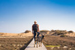 © satura_ - Man with dog walking on the wooden path on the beach and looking into the distance of the ocean