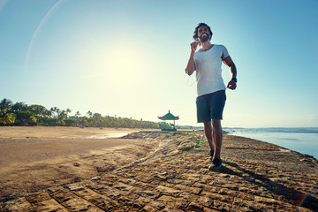 Wall Mural - Sports lifestyle. Happy young african man jogging on the sea shore.