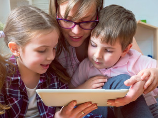 Mother, daughter and son sitting on floor, using tablet PC at home