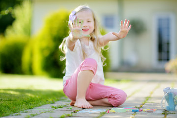 Cute little girl drawing with colorful chalks on a sidewalk. Summer activity for small kids.