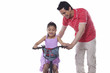 © IndiaPix - Father assisting daughter in riding bicycle over white background