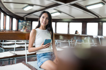 Wall Mural - Woman holding cellphone and looking out of window in ferry