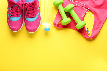 Wall Mural - Sport shoes with sportswear, dumbbells and bottle of water on yellow background